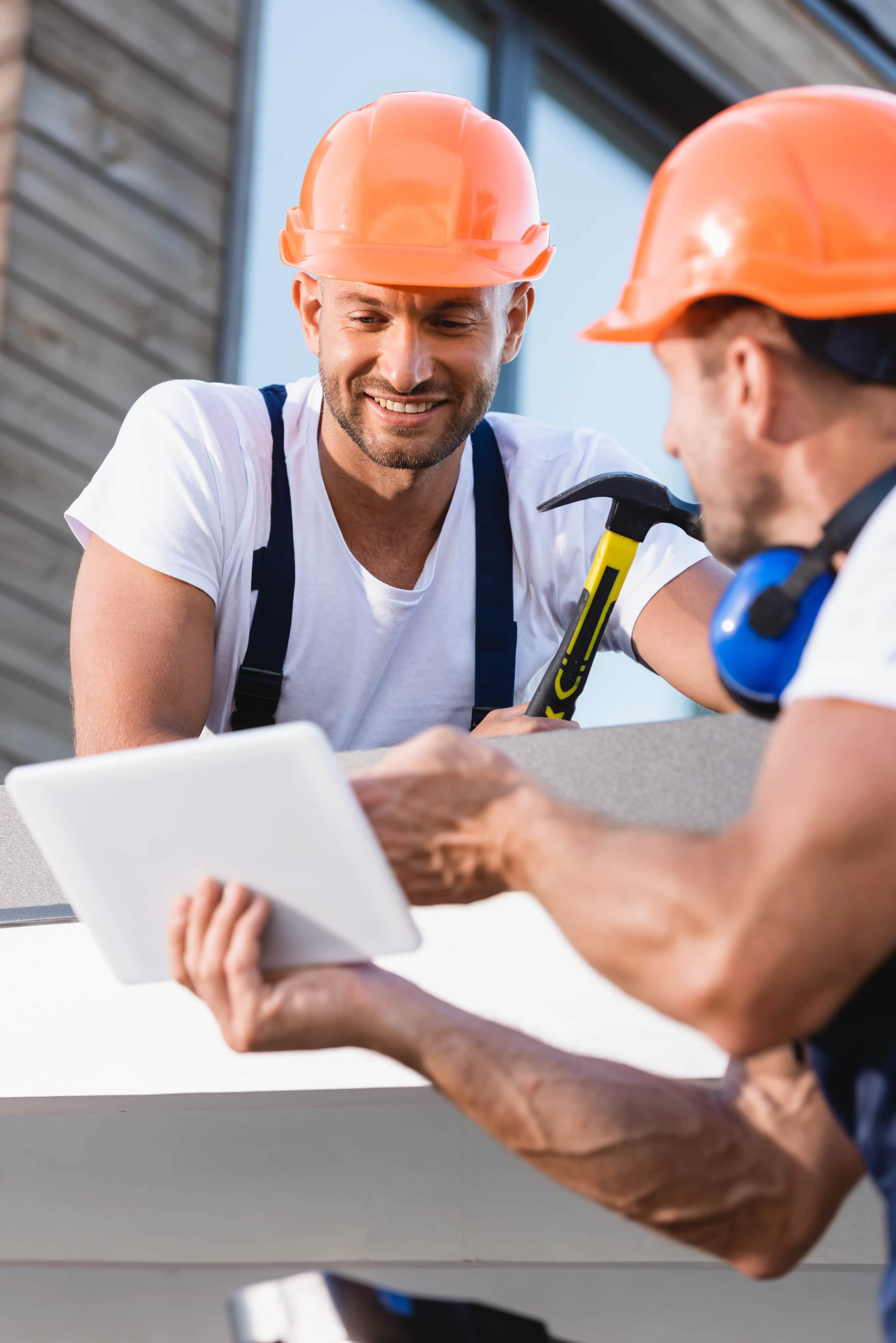 Builder holding a hammer while a colleague checks a digital tablet on a roofing project